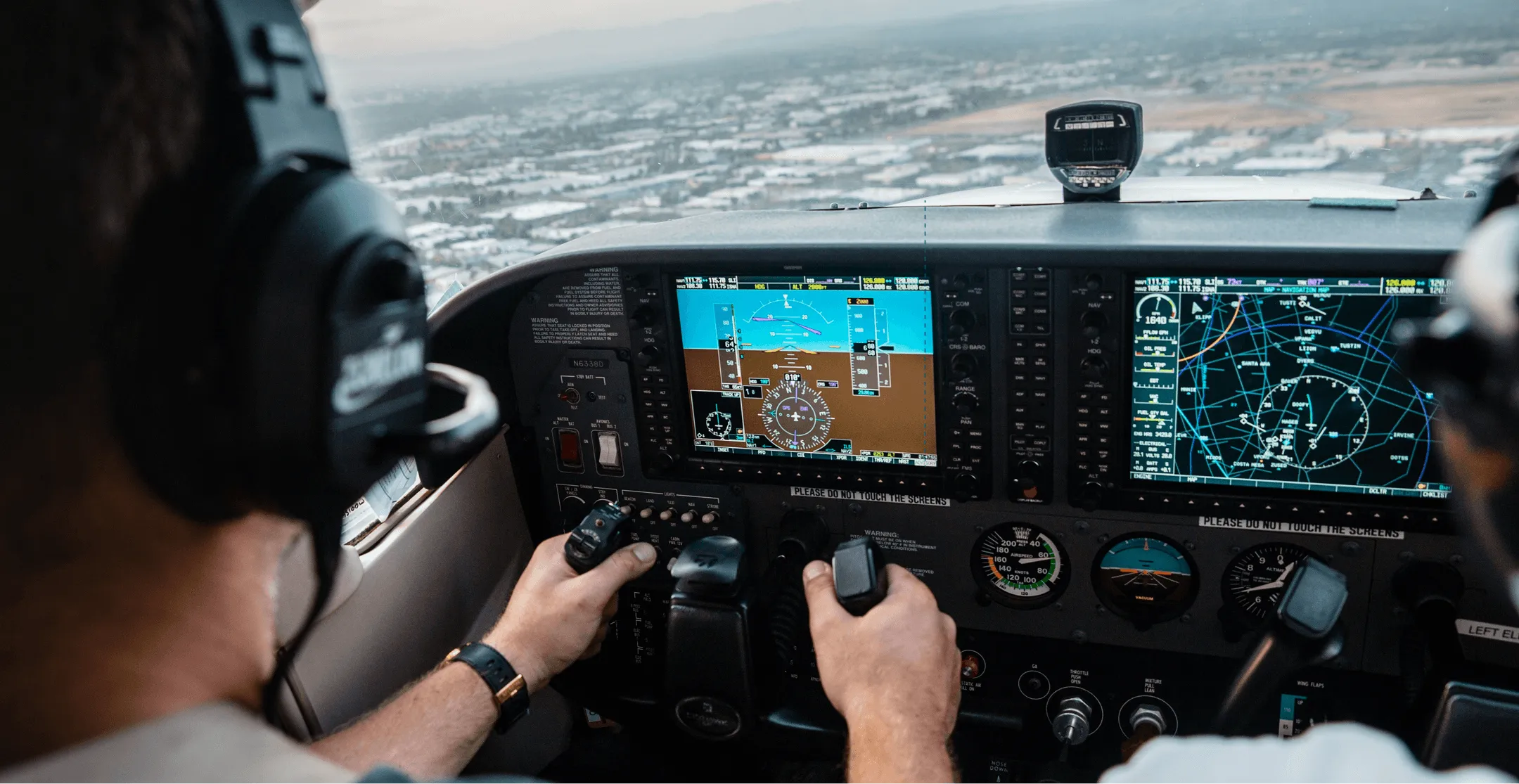 Pilot wearing headphones operating controls inside a small airplane cockpit with multiple digital flight instruments and navigation displays.