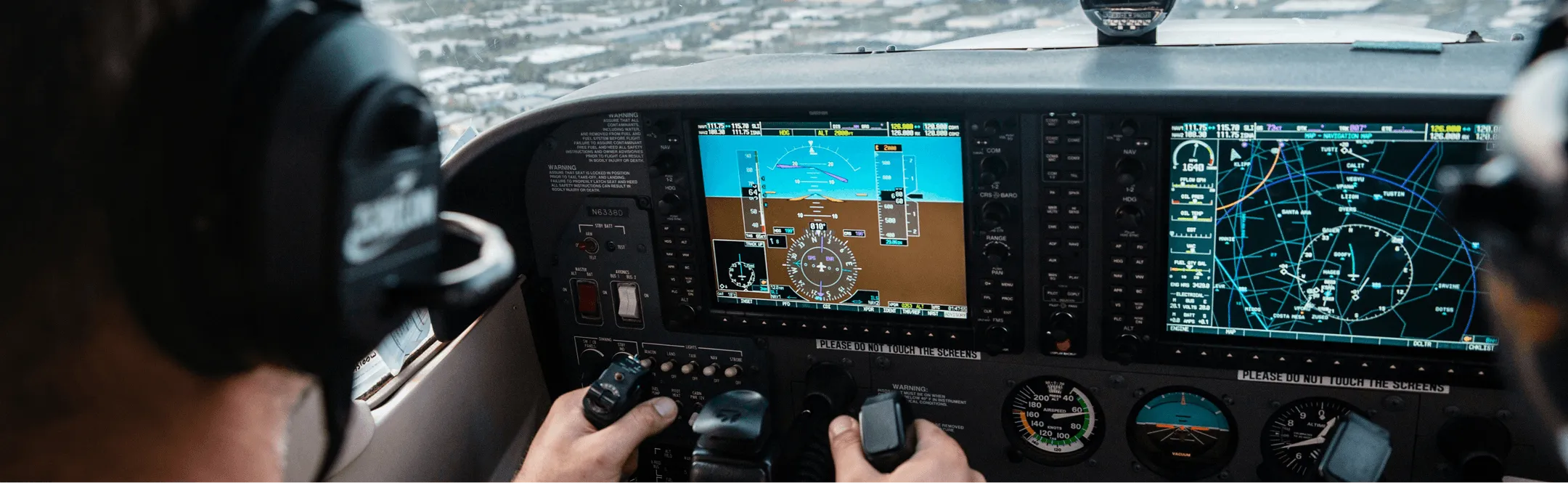 Pilot wearing headphones operating controls inside a small airplane cockpit with multiple digital flight instruments and navigation displays.