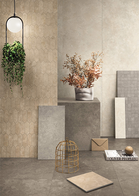 Interior scene with beige and gray decorative wall tiles, a hanging green plant, dried flower arrangement in a vase, and a book with an envelope and decorative objects on the floor.