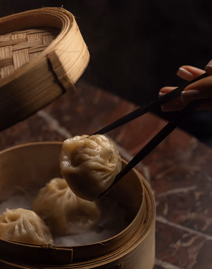 Chopsticks lifting a soup dumpling from a bamboo steamer at Mama Yo, Dublin