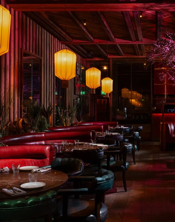 A triptych photograph of Mama Yo restaurant's interior, bathed in warm red and pink lighting. Cherry blossom branches cascade overhead, lanterns glow softly, and intimate seating is visible beneath the dramatic floral canopy, creating an immersive, moody Asian-inspired ambiance.