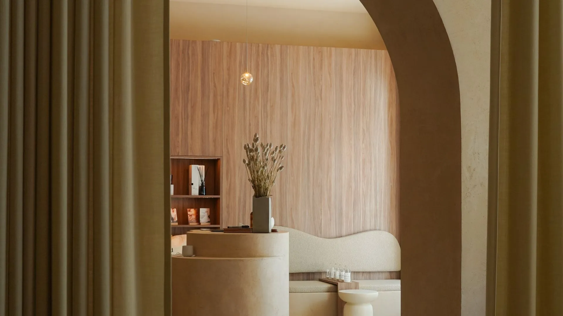 Modernes Interieur eines Soulhouse Studios mit hellen, organischen Formen, einer runden Theke, einer Vase mit getrockneten Blumen und einer Holzpaneelwand.