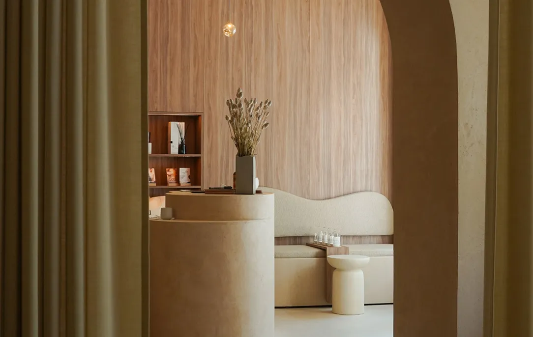 Minimalistischer Wartebereich in einem Soulhouse Studio mit rundem Empfangstresen, Sitzbank mit wellenförmiger Rückenlehne und hölzerner Wandverkleidung in neutralen Tönen.