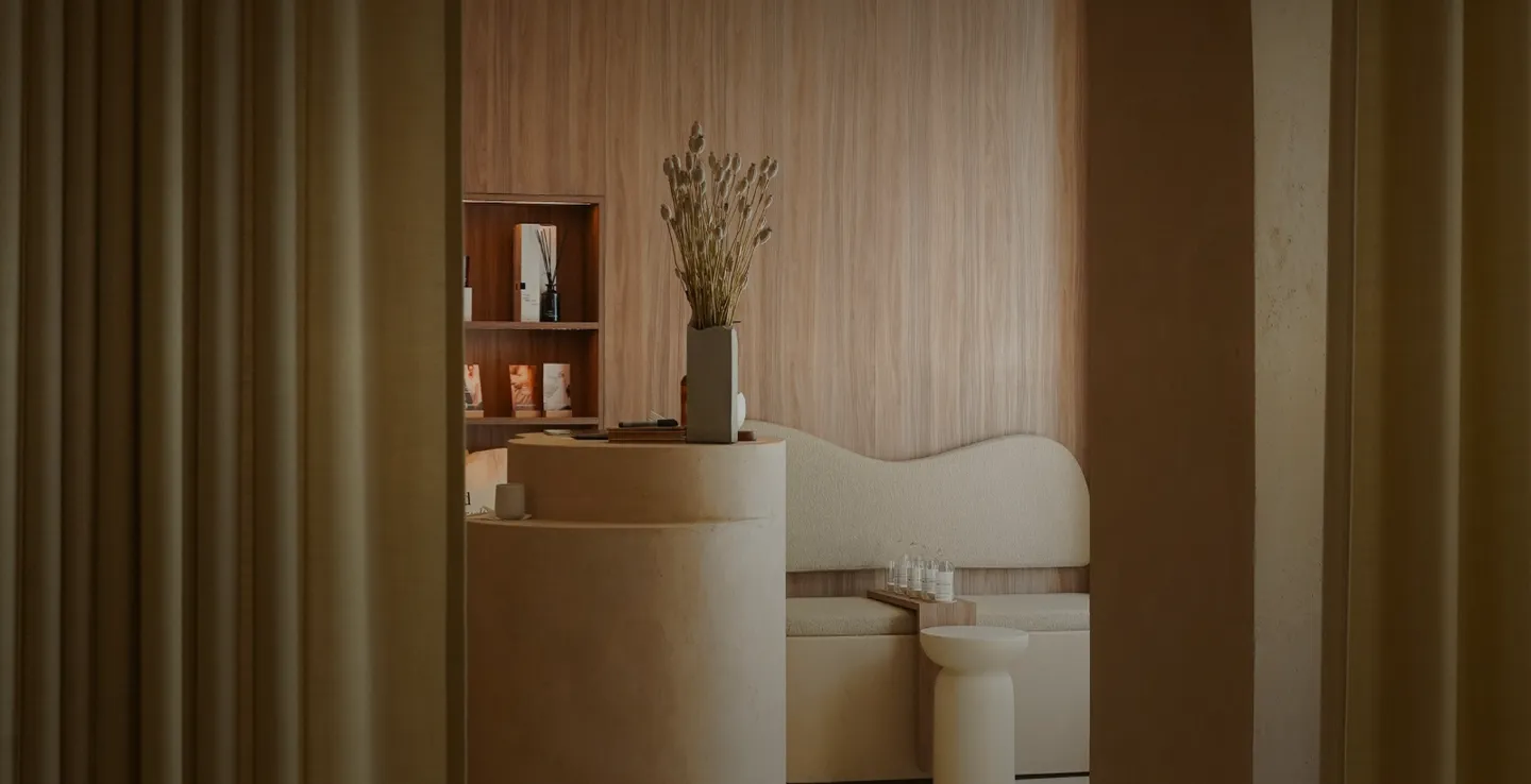 Minimalistisches Soulhouse Studio mit einer runden Säule, Vase mit Trockenblumen und geschwungener Sitzbank vor Holzwand.