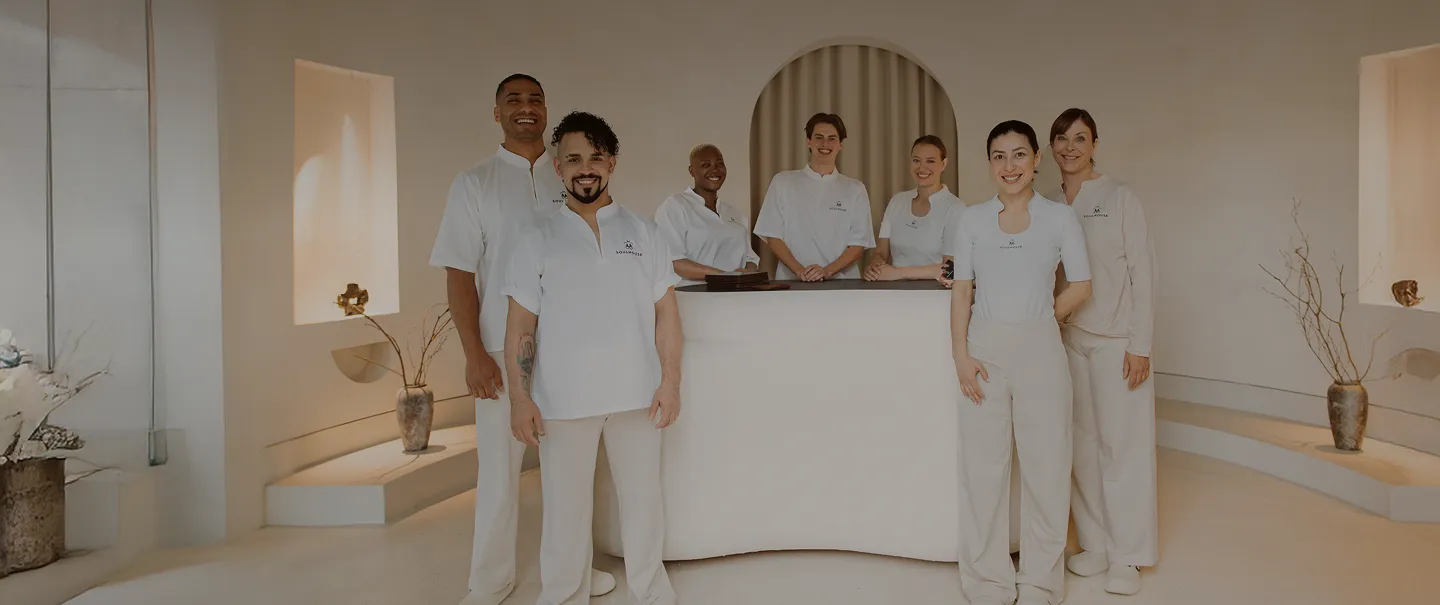 Ein Team von sieben freundlich lächelnden Soulhouse Experten in weißen Uniformen steht in einem modernen, hellen Empfangsbereich mit minimalistischer Dekoration.