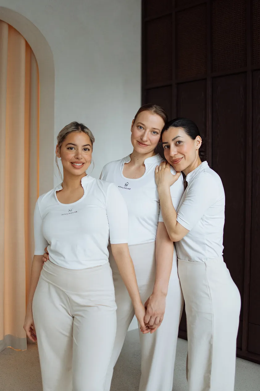 Gruppenbild von 3 Massageexpertinnen eng beieinander, zwei halten Händchen und eine lehnt ihren Kopf an die Schulter einer anderen.