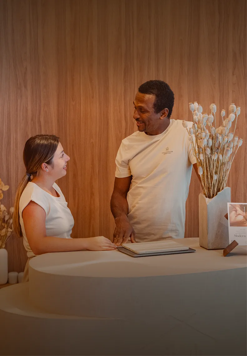 Zwei Soulhouse Experten, eine Frau und ein Mann, unterhalten sich lächelnd an einem schlichten Empfangstresen mit Holzvertäfelung im Hintergrund.