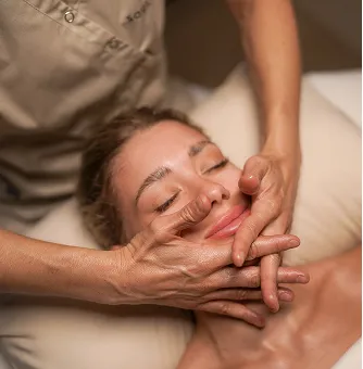 Frau erhält entspannende Lymphatic Face Glow Behandlung mit geschlossenen Augen, Hände des Massagetherapeuten drücken sanft das Gesicht.