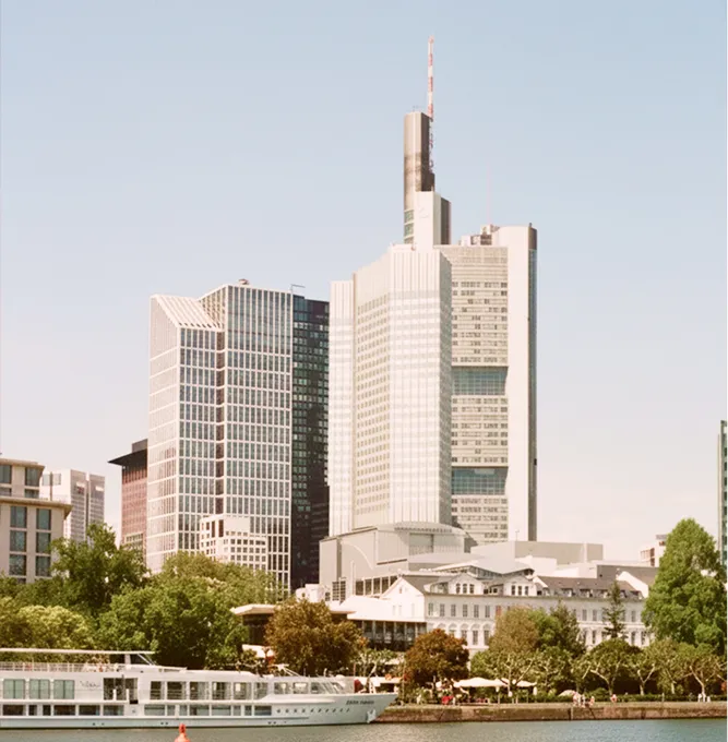 Moderne Wolkenkratzer und ältere Gebäude in Frankfurt am Main mit einem weißen Passagierschiff im Vordergrund unter klarem Himmel.