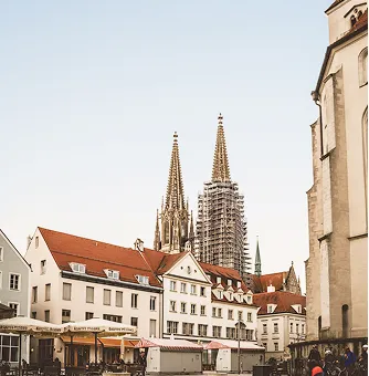 Historische Gebäude mit spitzen Kirchtürmen und roten Dächern unter klarem Himmel in einer europäischen Stadt.