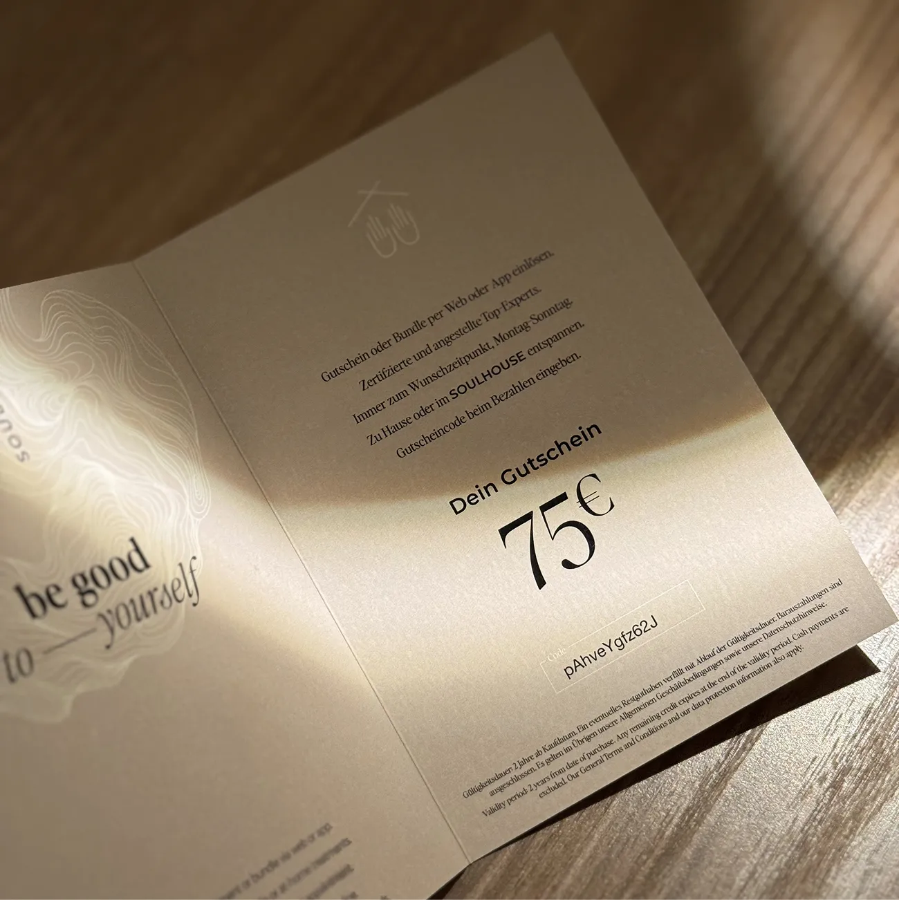 Ein Soulhouse Gutschein im Wert von 75 Euro auf einem aufgeschlagenen hellen Papier mit Text über Einlösung und einem Gutscheincode.