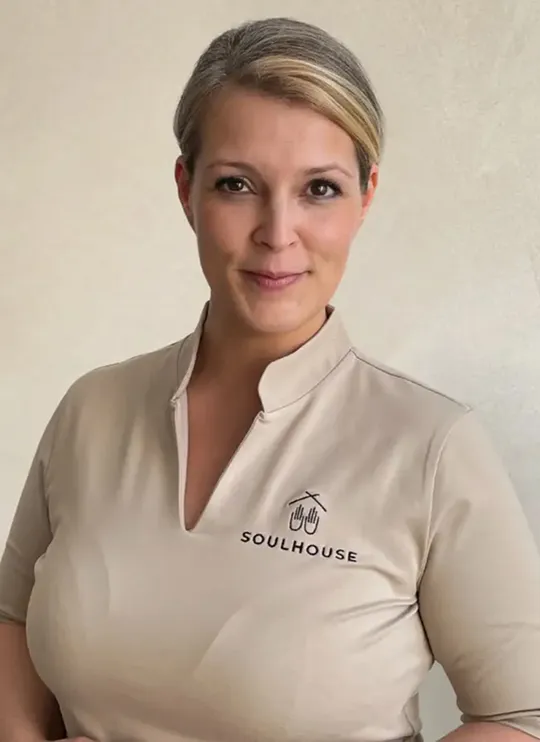 Soulhouse Massage Expertin mit zurückgebundenem Haar, die ein beiges Oberteil mit dem Logo und Schriftzug 'Soulhouse' trägt.