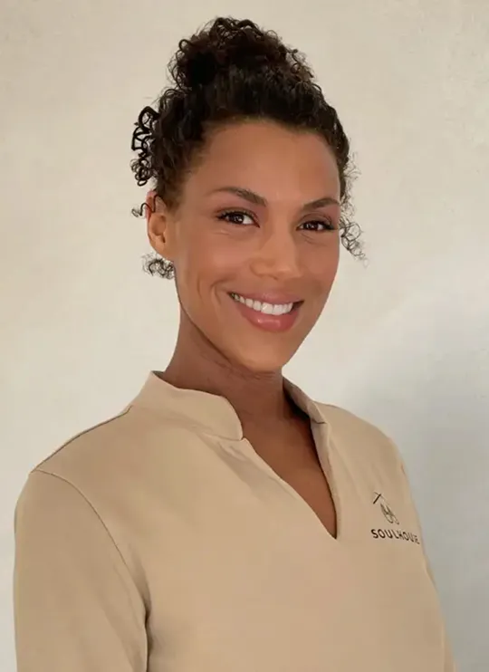 Soulhouse Massage Expertin mit zusammengebundenen Locken trägt hellbeige Oberteil.