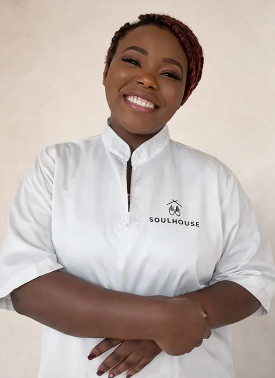 Soulhouse Massage Expertin mit geflochtenem Haar trägt weißes Oberteil mit dem Logo 'SOULHOUSE'.
