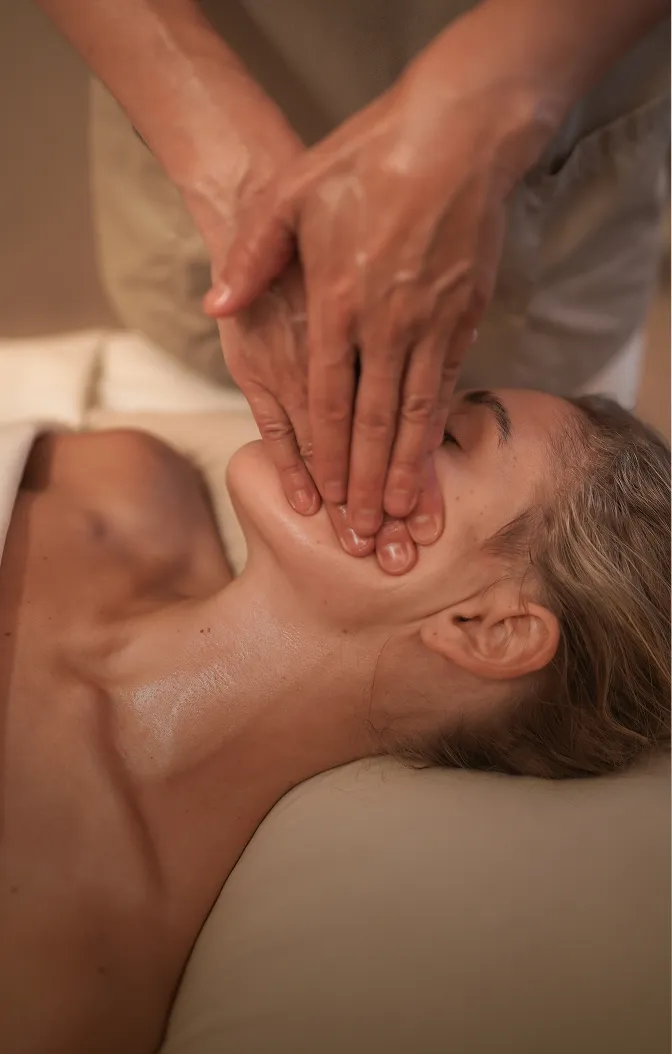 Frau entspannt sich bei einer Gesichts- und Nackenmassage mit geölten Händen.