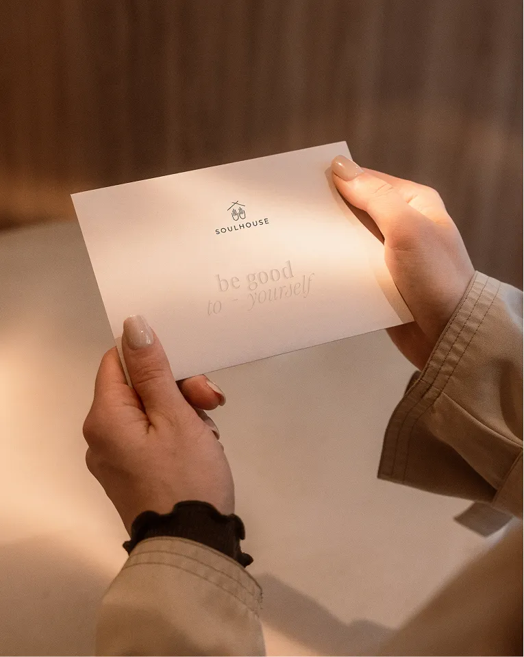 Person hält einen Gutschein mit der Aufschrift ‚Soulhouse‘ und dem Text ‚be good to yourself‘.