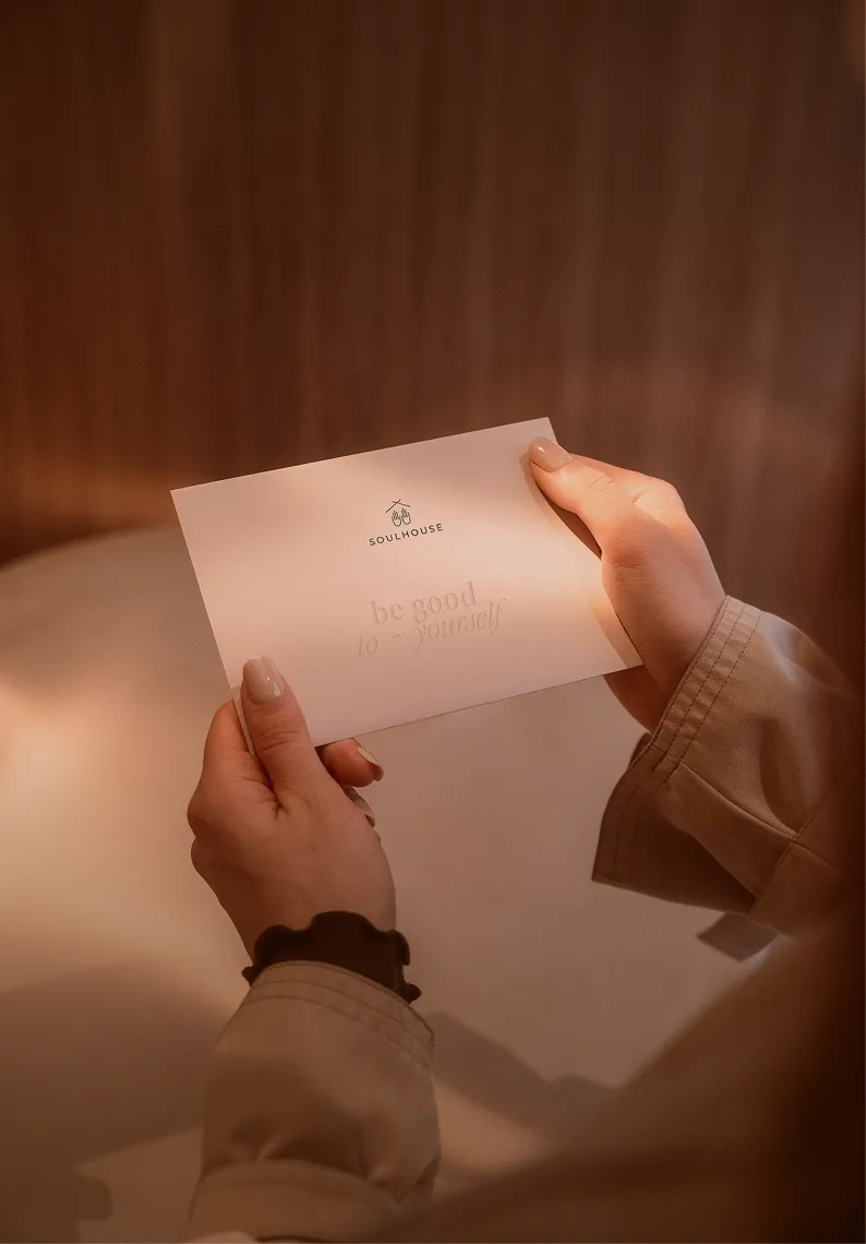 Hände halten einen Soulhouse Gutschein mit dem Text 'Soulhouse' und 'be good to yourself'.