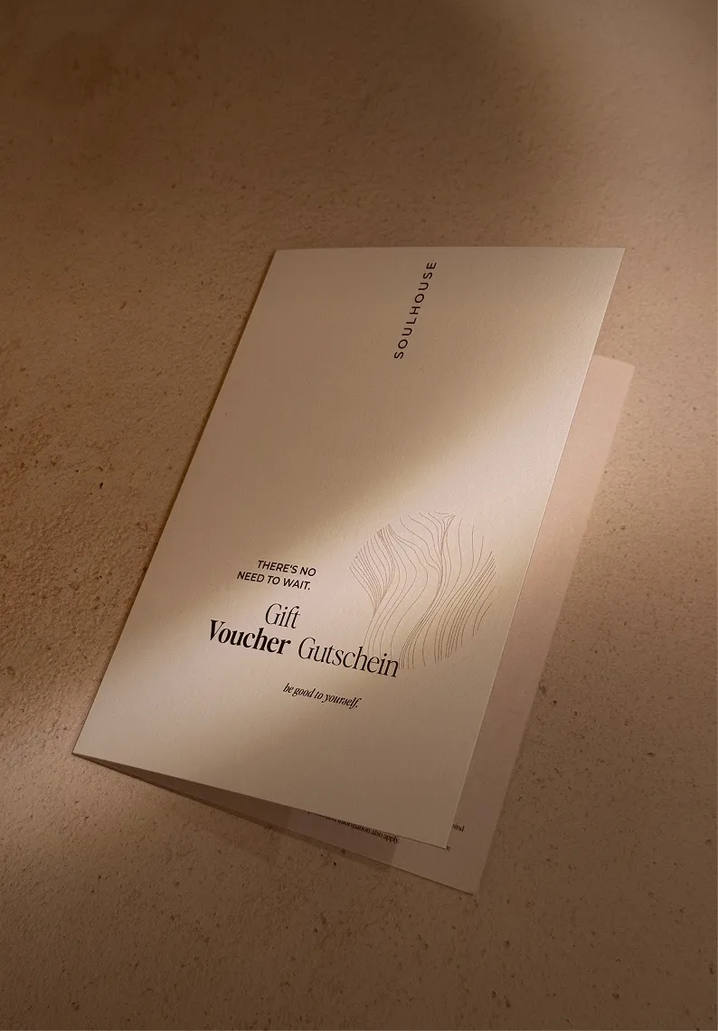 Ein minimalistischer Geschenkgutschein der Marke Soulhouse auf einem beigen Untergrund mit dem Text 'Es gibt keinen Grund zu warten. Geschenkgutschein. Sei gut zu dir selbst.'