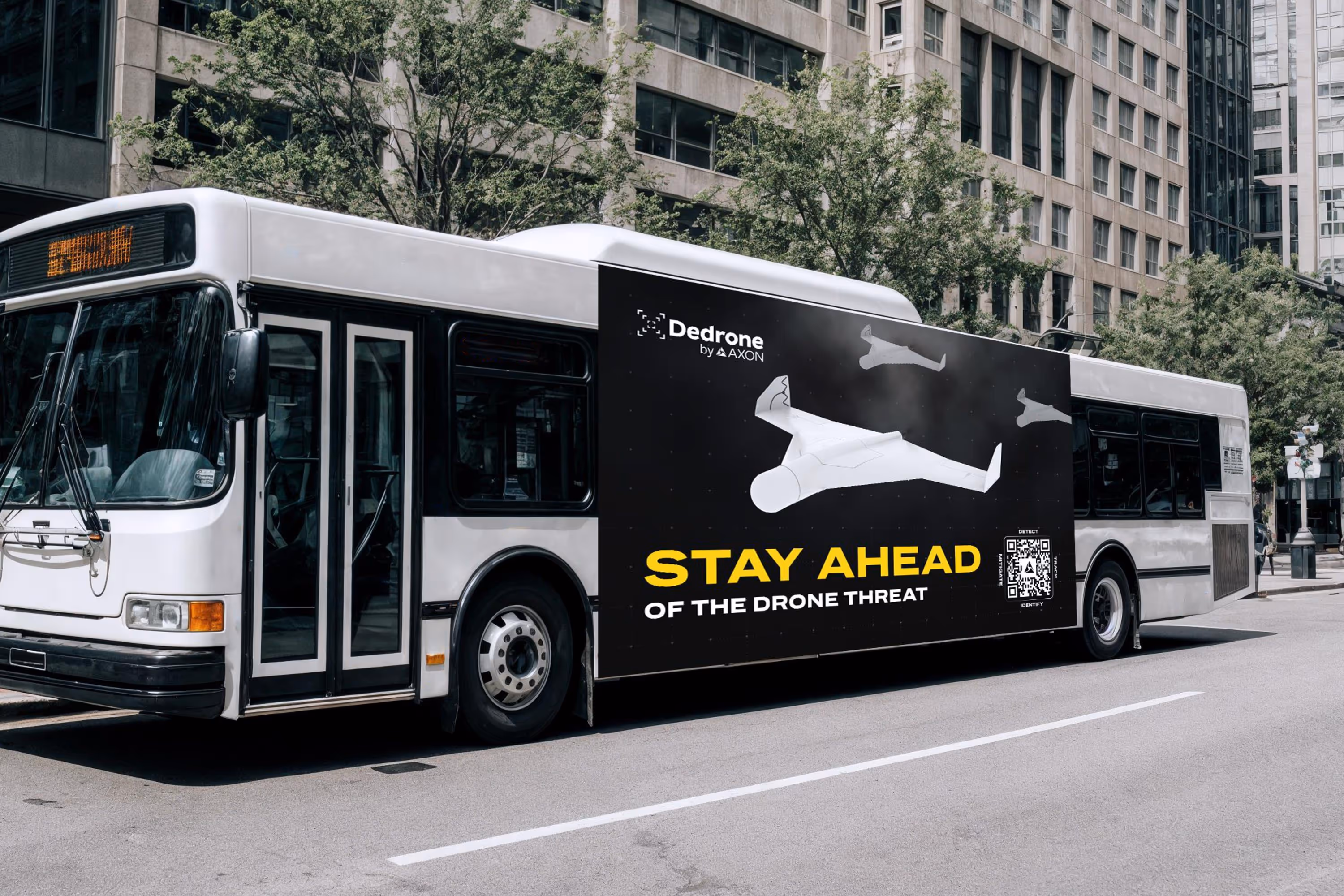 White city bus with a large black advertisement on its side showing drone illustrations and text 'Stay Ahead of the Drone Threat' by Dedrone.