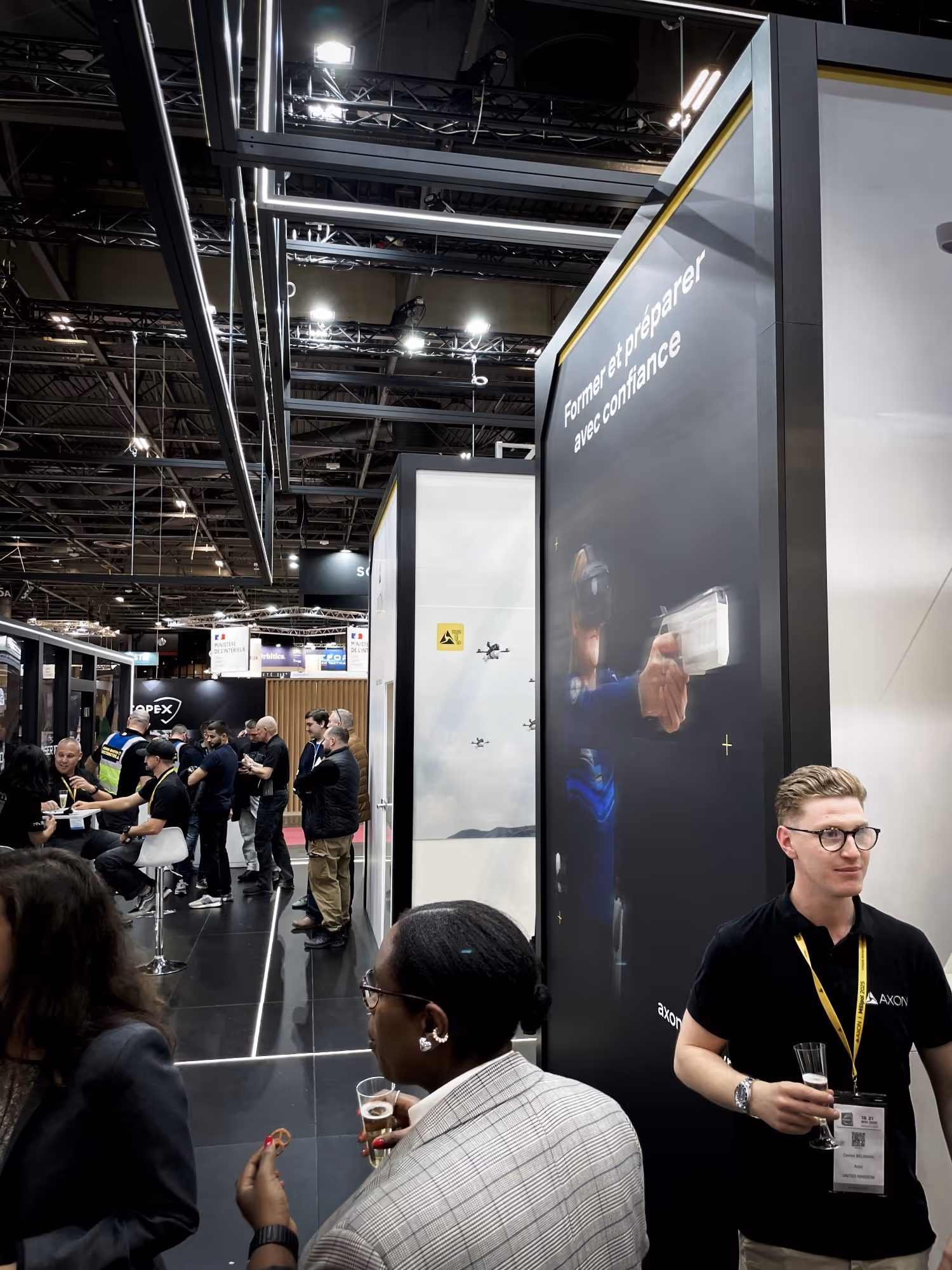 Two soldiers in tactical gear aiming rifles behind a protective digital shield as three drones fly in dark smoky sky.