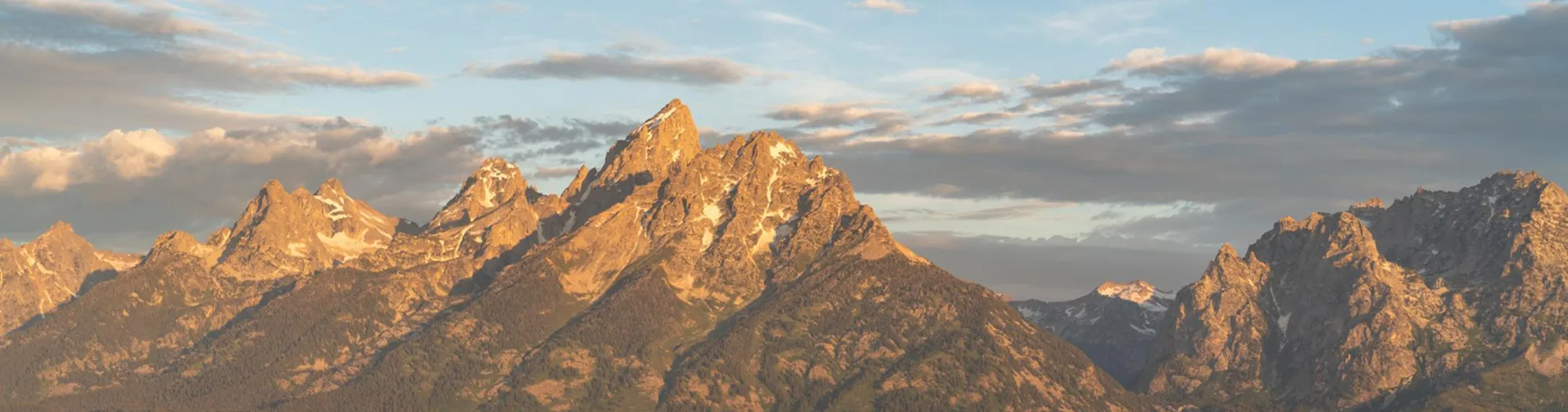 Mountain range illuminated by warm sunlight under a partly cloudy sky.