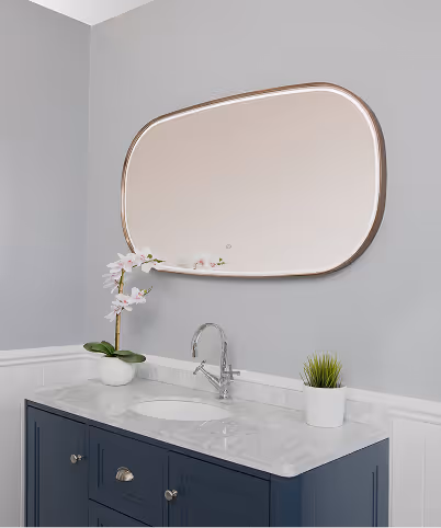 Bathroom vanity with navy blue cabinet, white marble countertop, oval sink, curved mirror, white orchid, and small potted plant against light gray wall.