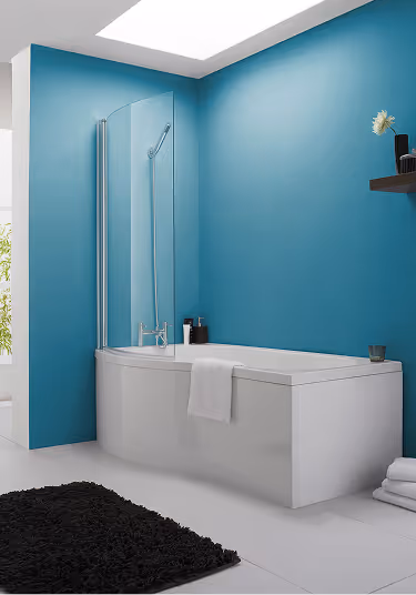 Modern white bathtub with a glass shower screen against a teal bathroom wall and a black rug on the floor.