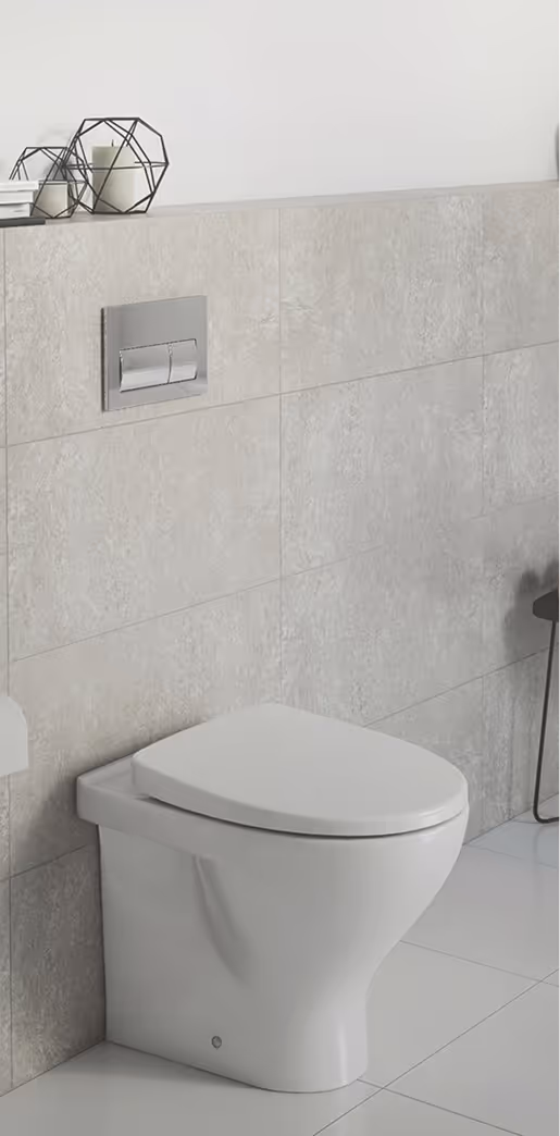 Modern white toilet with closed lid against beige tiled wall featuring a dual flush chrome button panel, with decorative candle holders on the ledge above.