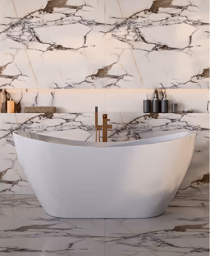 Modern white freestanding bathtub with gold faucet against marble wall and floor with black and brown veins.