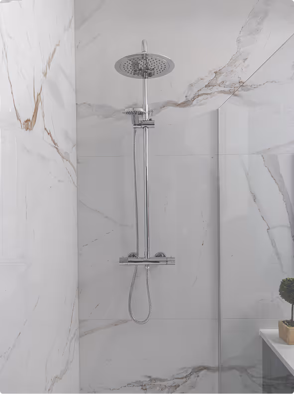 Modern shower with a round rain showerhead and handheld shower on a chrome bar, set against white marble walls with gray and brown veining.