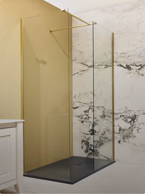 Modern walk-in shower with black tray, clear glass panels framed in gold, and marble wall tiles.