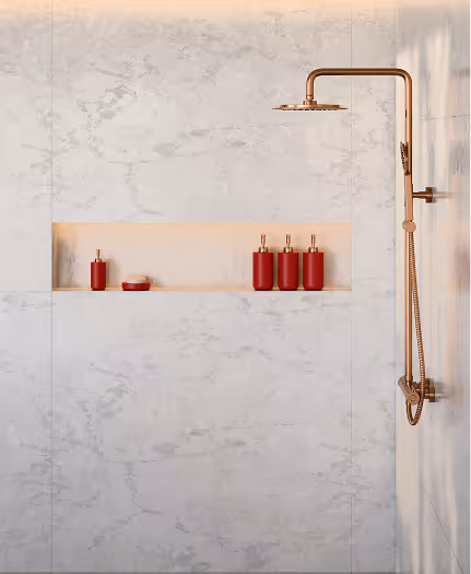 Modern shower with a rose gold rain showerhead and four red toiletry bottles on a recessed shelf in white marble tiled wall.