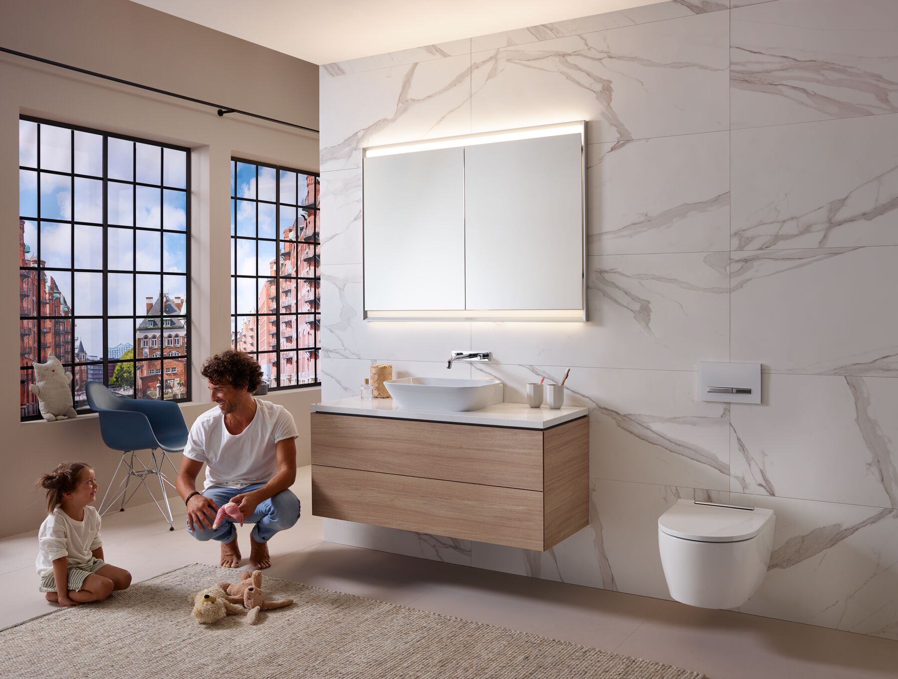 Man and young girl playing with stuffed animals on rug in a modern bathroom with large windows, floating vanity, and wall-mounted toilet.