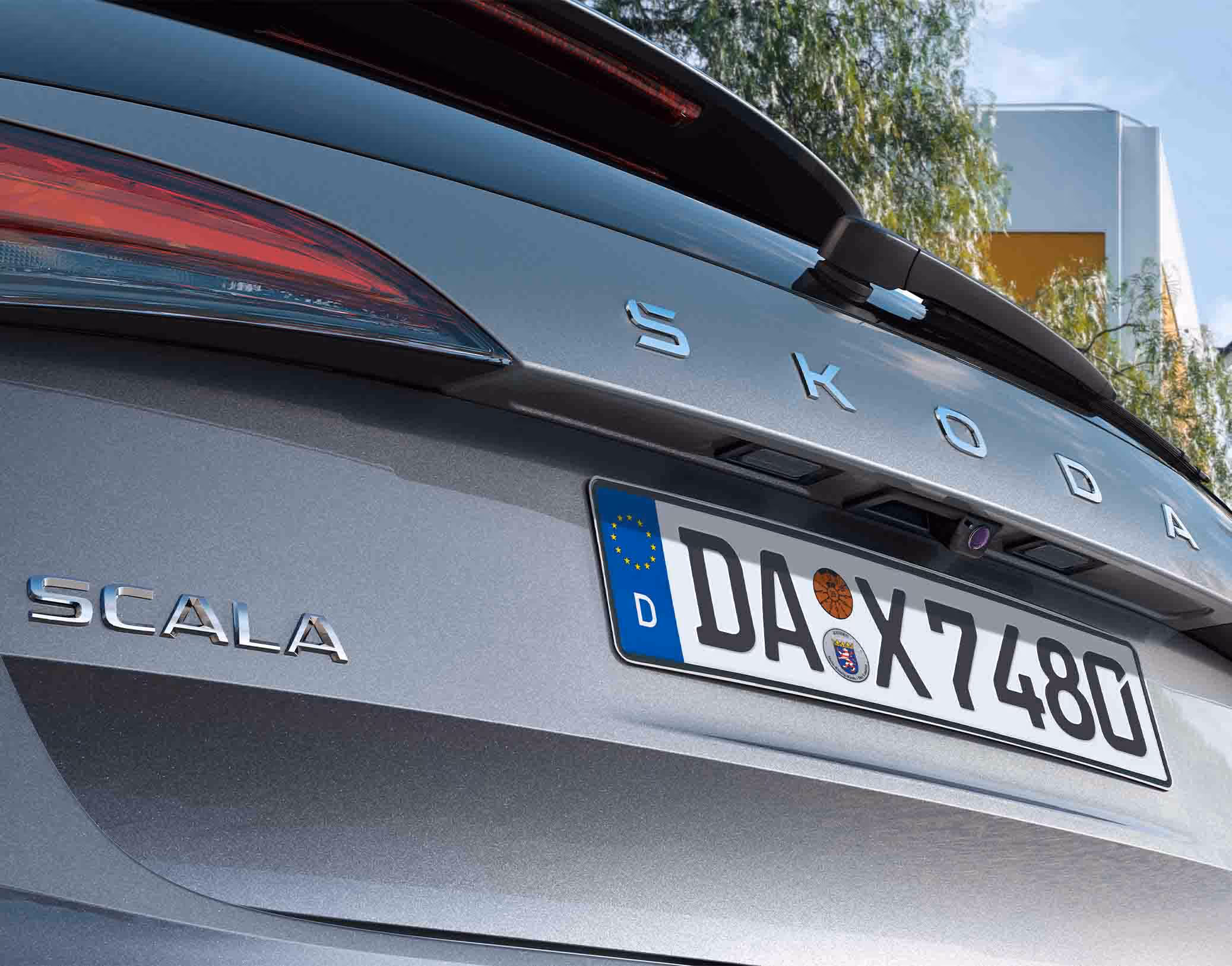 Detailaufnahme der Heckpartie eines Škoda Scala Balance in der Lackierung Graphite-Grau Metallic. Der Fokus liegt auf der integrierten Rückfahrkamera, die zentral über dem Kennzeichen platziert ist. Zudem sind die verchromten Schriftzüge „ŠKODA“ und „SCALA“ auf der Heckklappe deutlich zu erkennen.