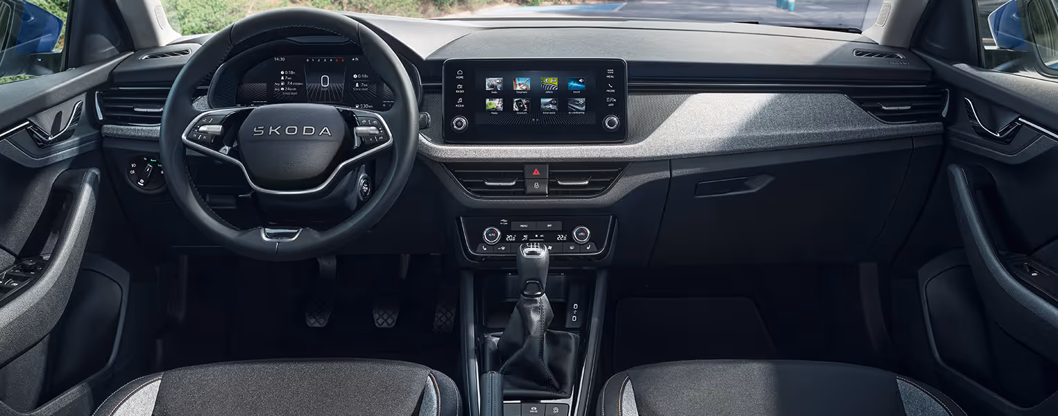 Blick in das Interieur des Škoda Scala Balance mit Fokus auf das Cockpit und das Armaturenbrett mit grauer Stoff-Dekorleiste. Das Bild zeigt das 2-Speichen-Multifunktionslenkrad vor dem digitalen Kombiinstrument sowie das zentral angeordnete Infotainment-Display. Grüne Plus-Symbole heben interaktive Bereiche auf dem Bild hervor.