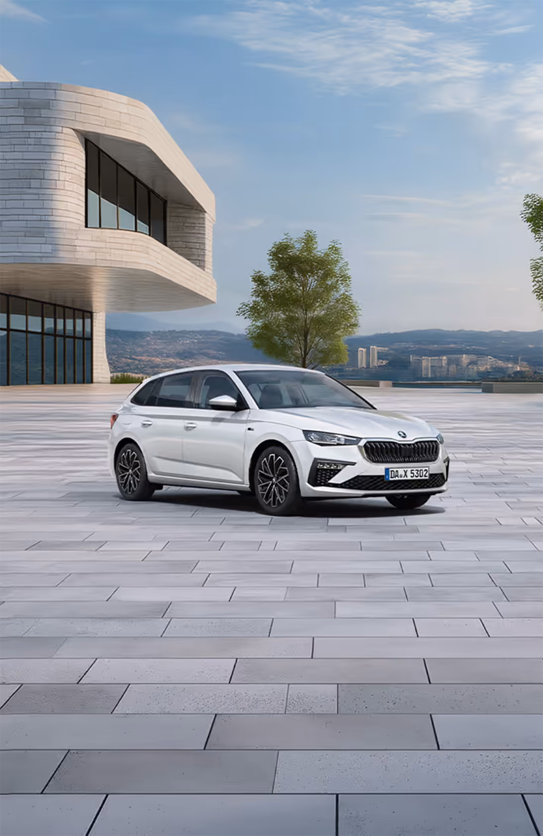 Front-Schrägansicht des Škoda Scala Balance in der Lackierung Moon-Weiß Perleffekt auf einem gepflasterten Platz vor einer Stadtkulisse in der Ferne. Das Fahrzeug ist mit dunklen, glanzgedrehten Leichtmetallfelgen ausgestattet. Im unteren Bildbereich weist ein grüner Störer auf einen Preisvorteil von 2.100 € sowie die inkludierte 5-Jahres-Garantie hin.