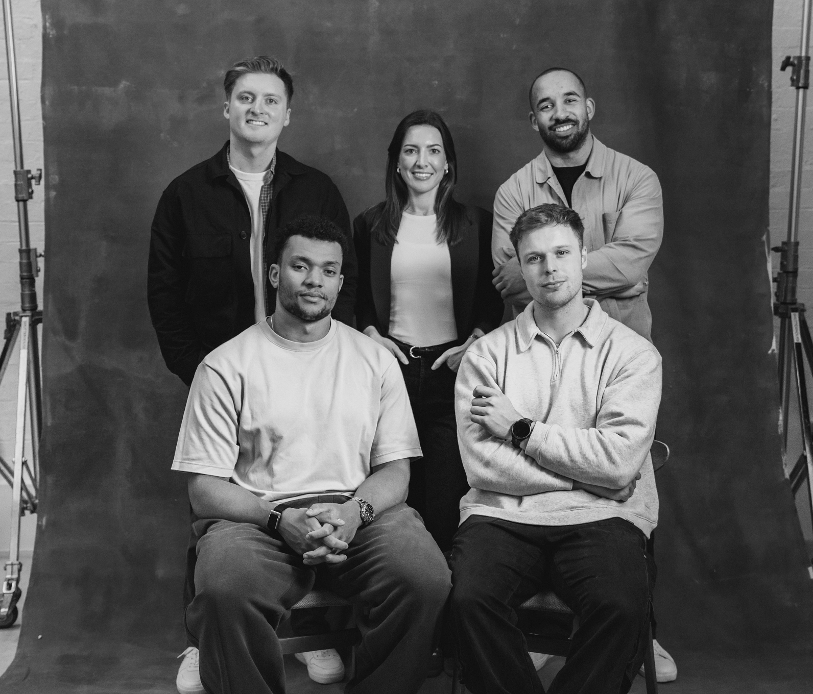 Black and white photo of five adults, three standing and two seated, posing in front of a plain backdrop.