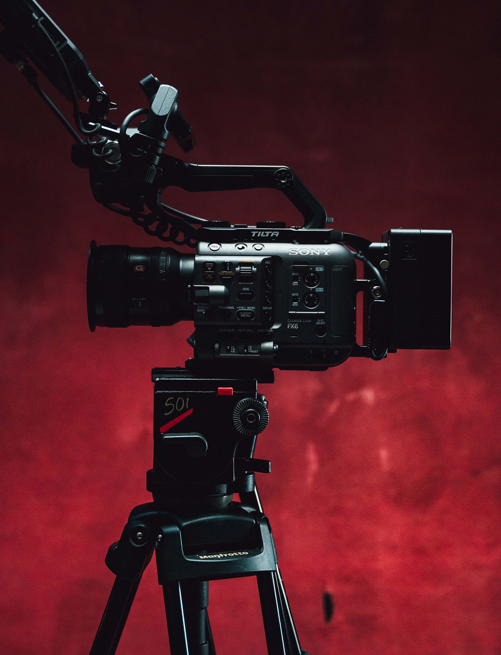 Professional Sony FX6 cinema camera mounted on a Manfrotto tripod against a dark red background.