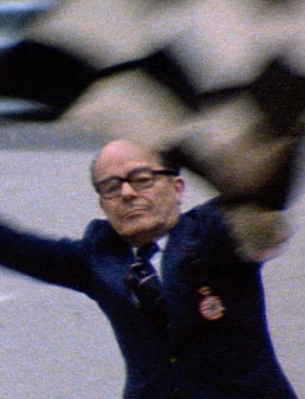 Man in glasses and a dark blazer with a crest throwing or catching a brown and black bird in motion.