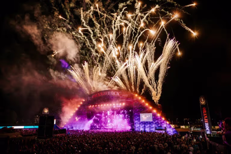 Vuurwerk gaat af boven een goed bezocht podium tijdens een nachtelijk muziekfestival.