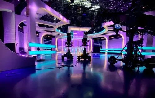 Moderne televisiestudio met paars en blauw neonlicht, camerasteigers en een glanzende vloer.