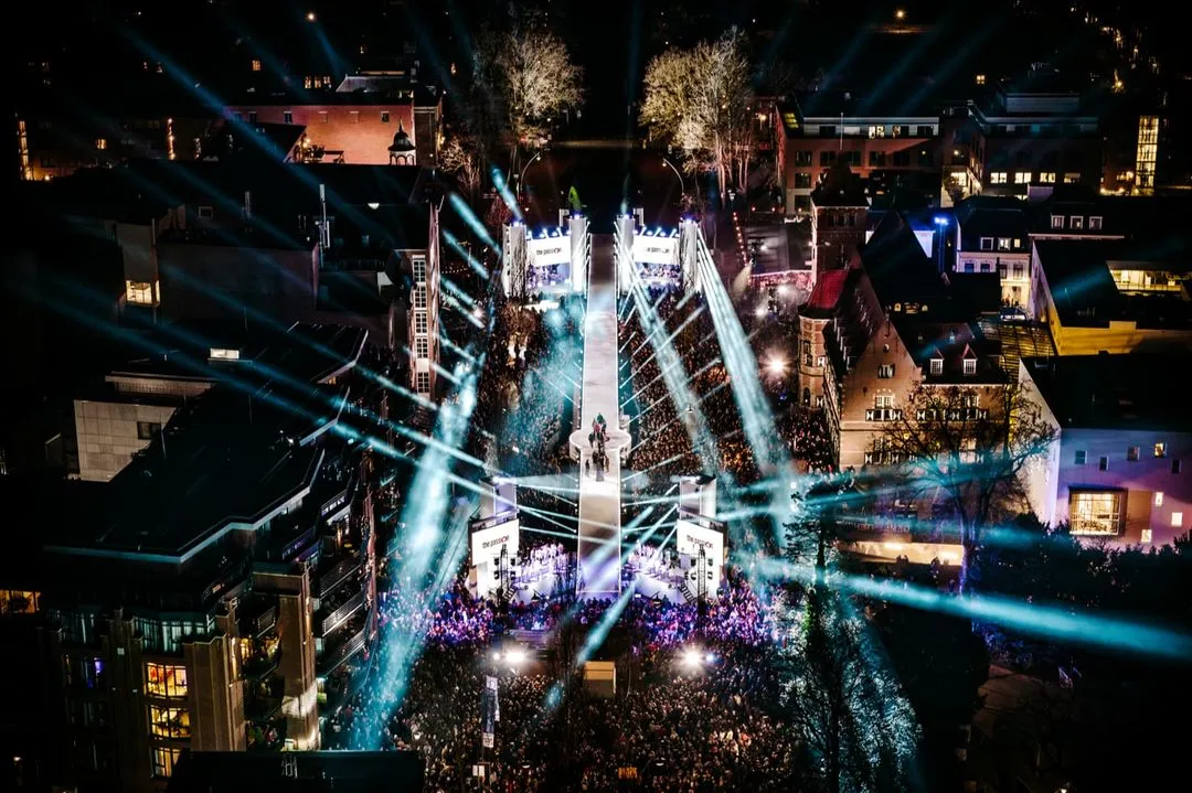 Nachtluchtfoto van evenement The Passion met felblauwe en witte lichtstralen die het publiek en het podium verlichten.