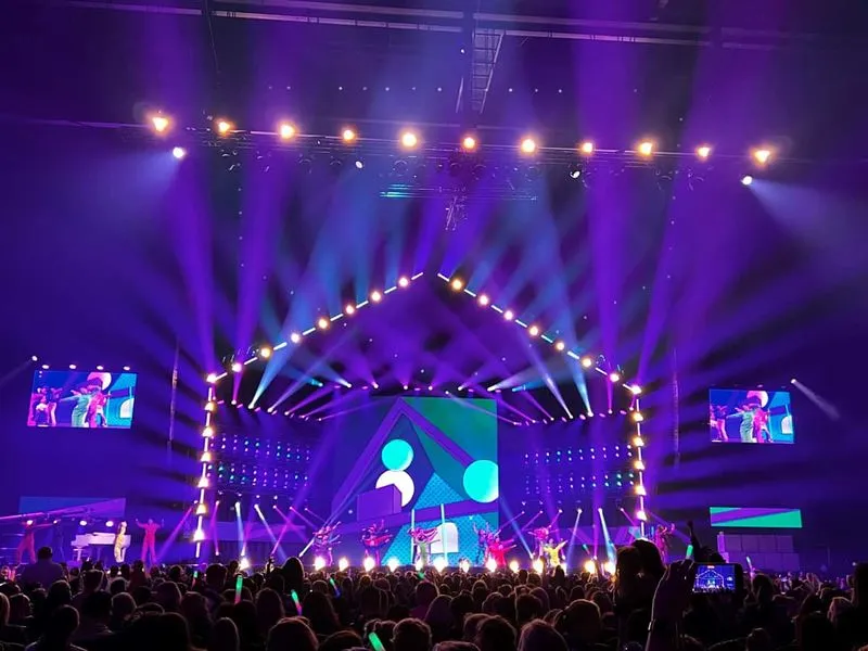 Podium met kleurrijke dansers en felpaarse en blauwe lichten tijdens een drukbezocht evenement.