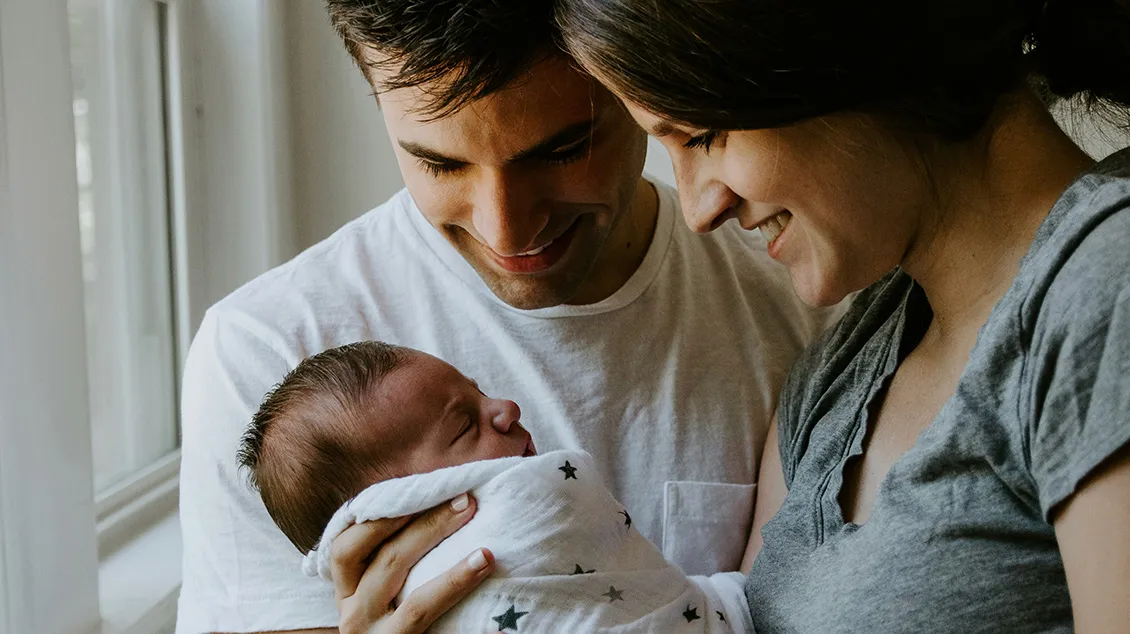 Mother and father smiling and looking lovingly at their newborn baby wrapped in a star-patterned blanket.
