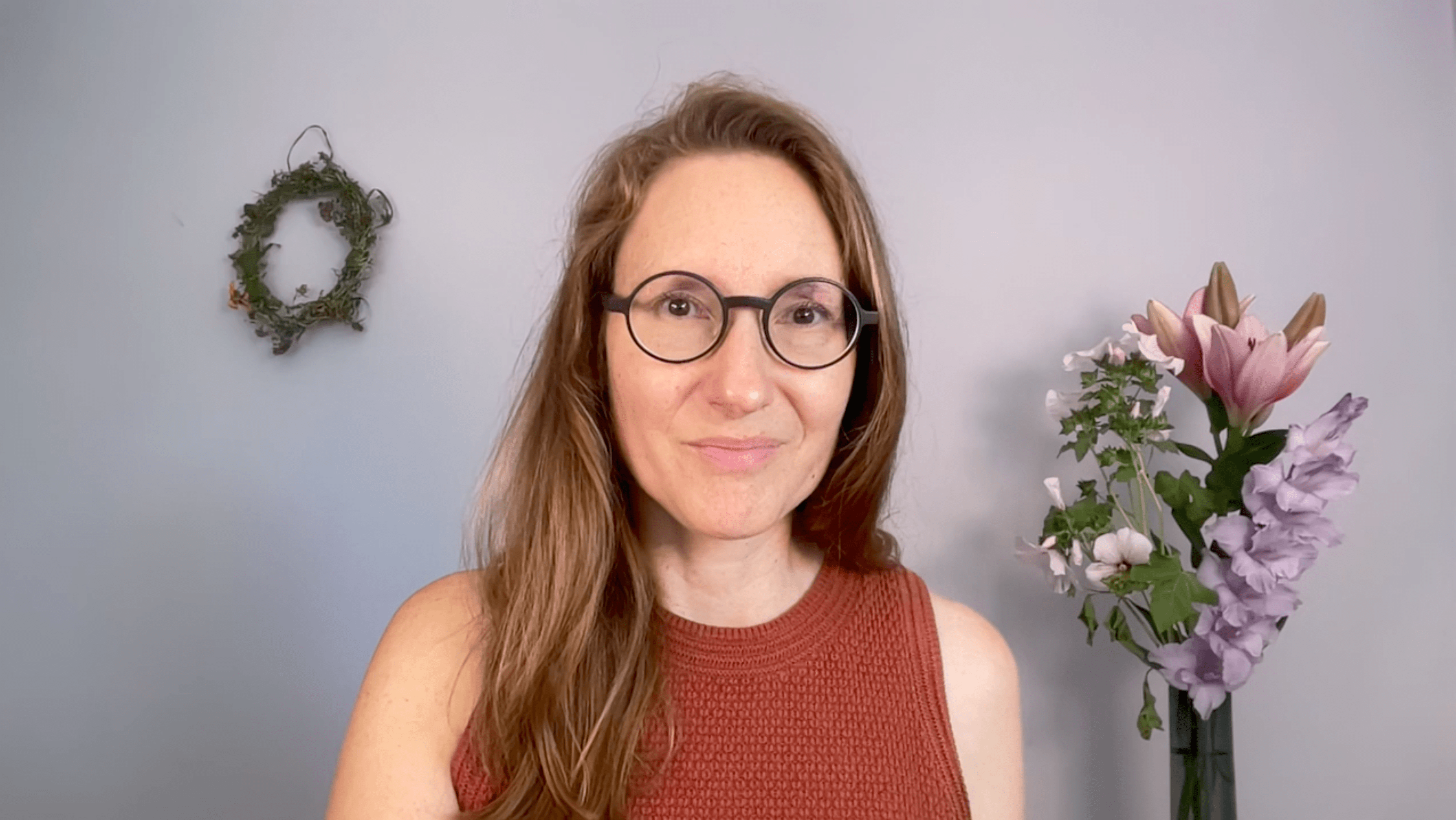 Woman with long brown hair and round glasses wearing a rust-colored sleeveless top.