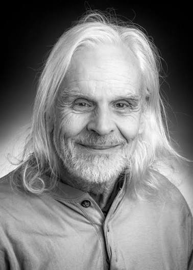 Smiling elderly man with long white hair and beard in a black and white portrait.