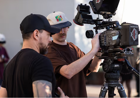 Two video production crew members adjusting a professional cinema camera on set