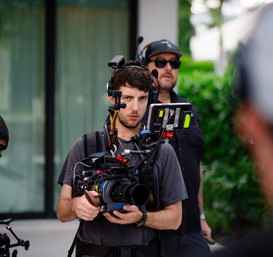 Camera operator holding cinema camera rig on TV commercial set, boom mic operator behind him.