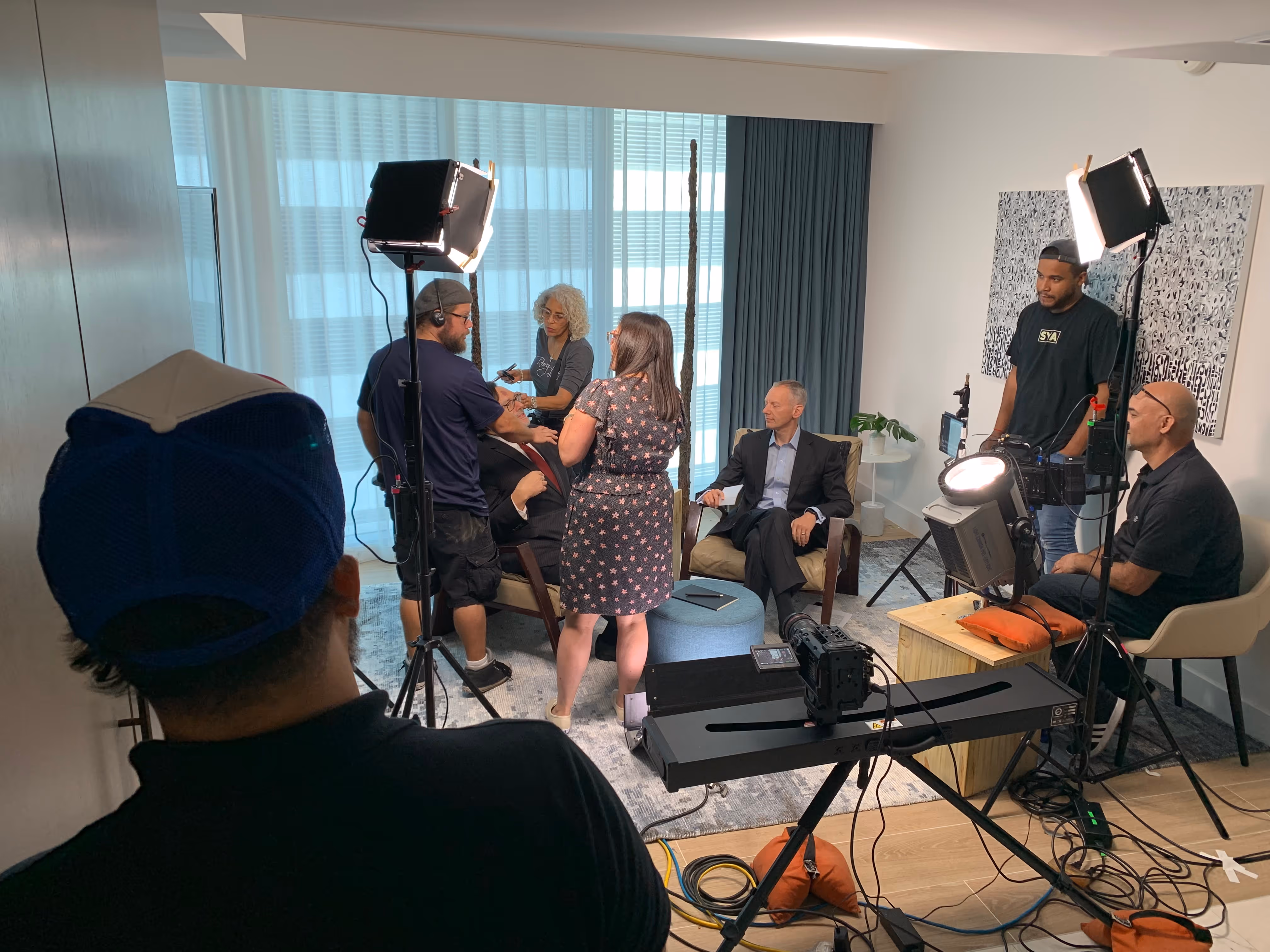 Corporate interview pre-production setup with crew, lighting, and interview subject in hotel room