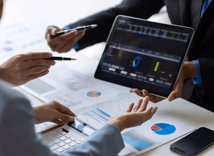 Two people in business attire reviewing financial charts on paper and a tablet displaying data visualizations.